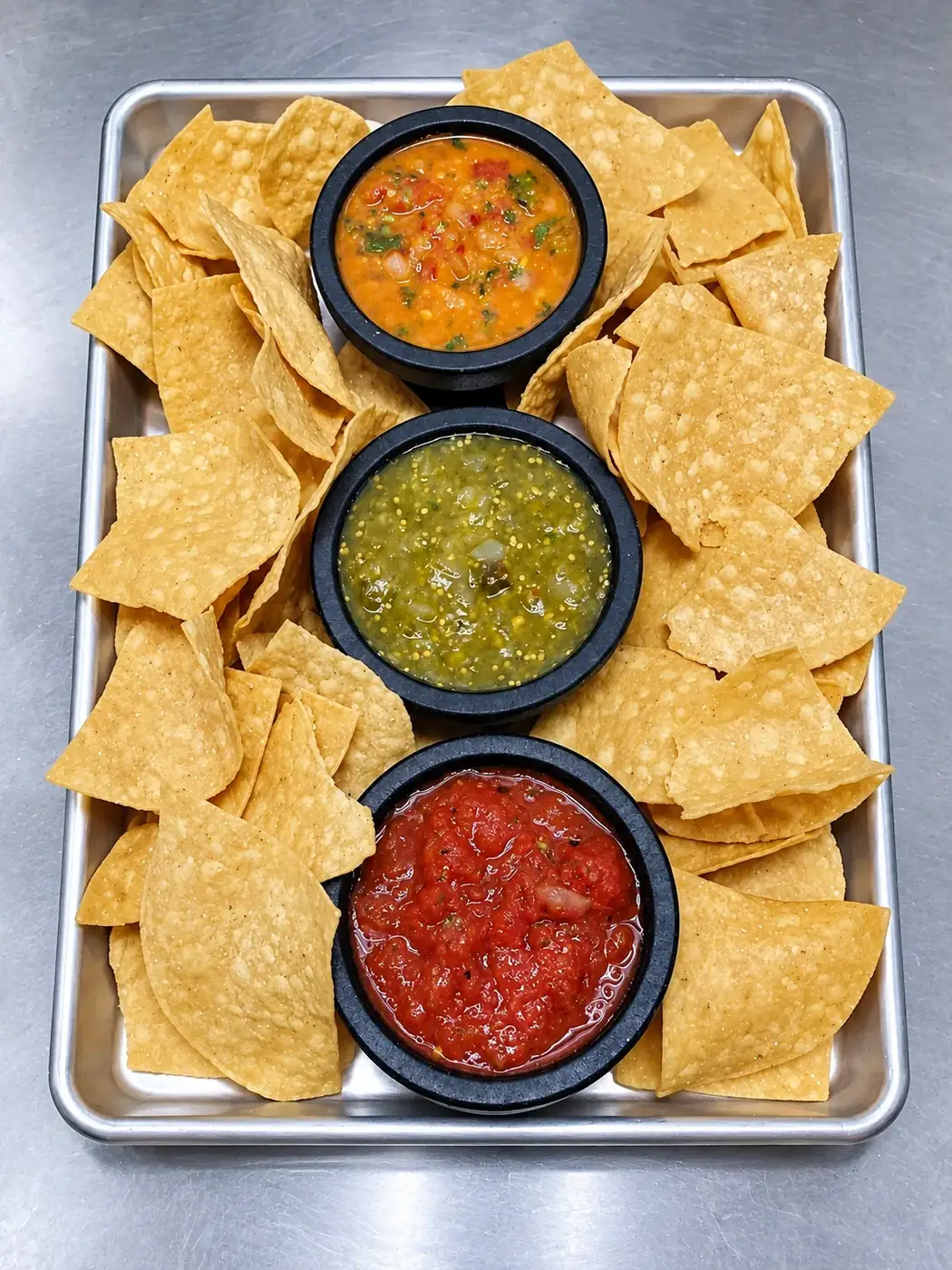 Complete tray of tortilla chips with orange, green and red salsa